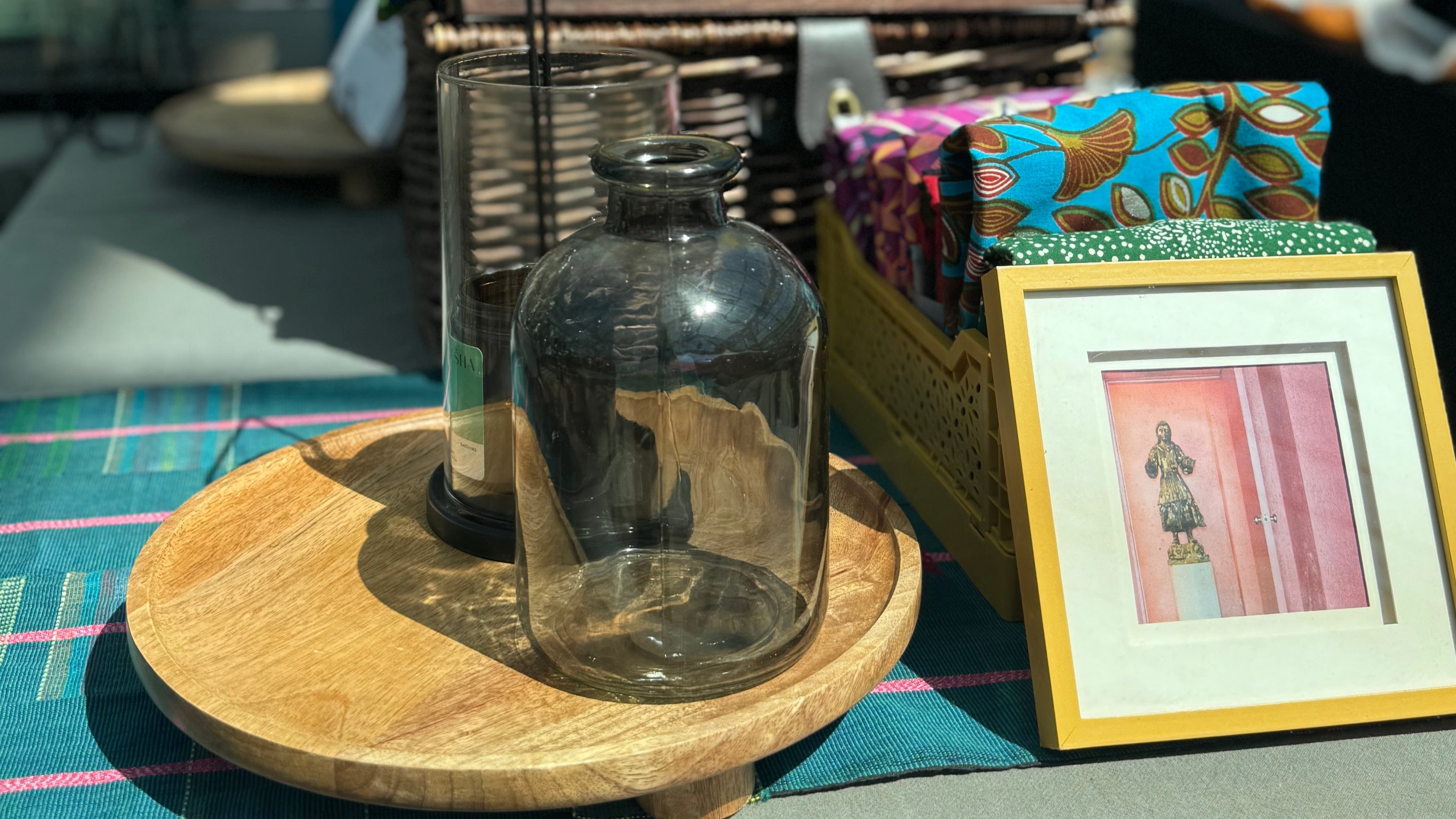 Colorful leaf-patterned cushion on a chair with a glass bottle and framed picture on a table.